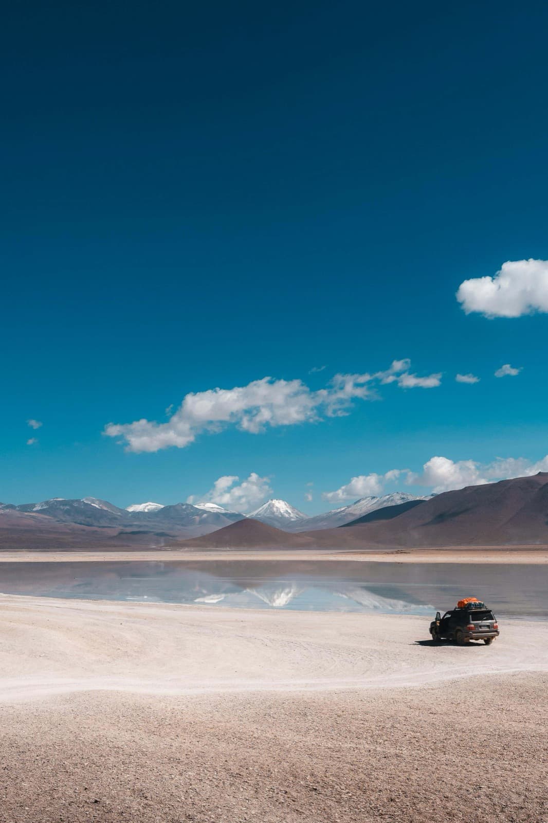 High-altitude lagoon and snow-capped mountains of Sud Lípez with a 4x4 on the shore in Bolivia