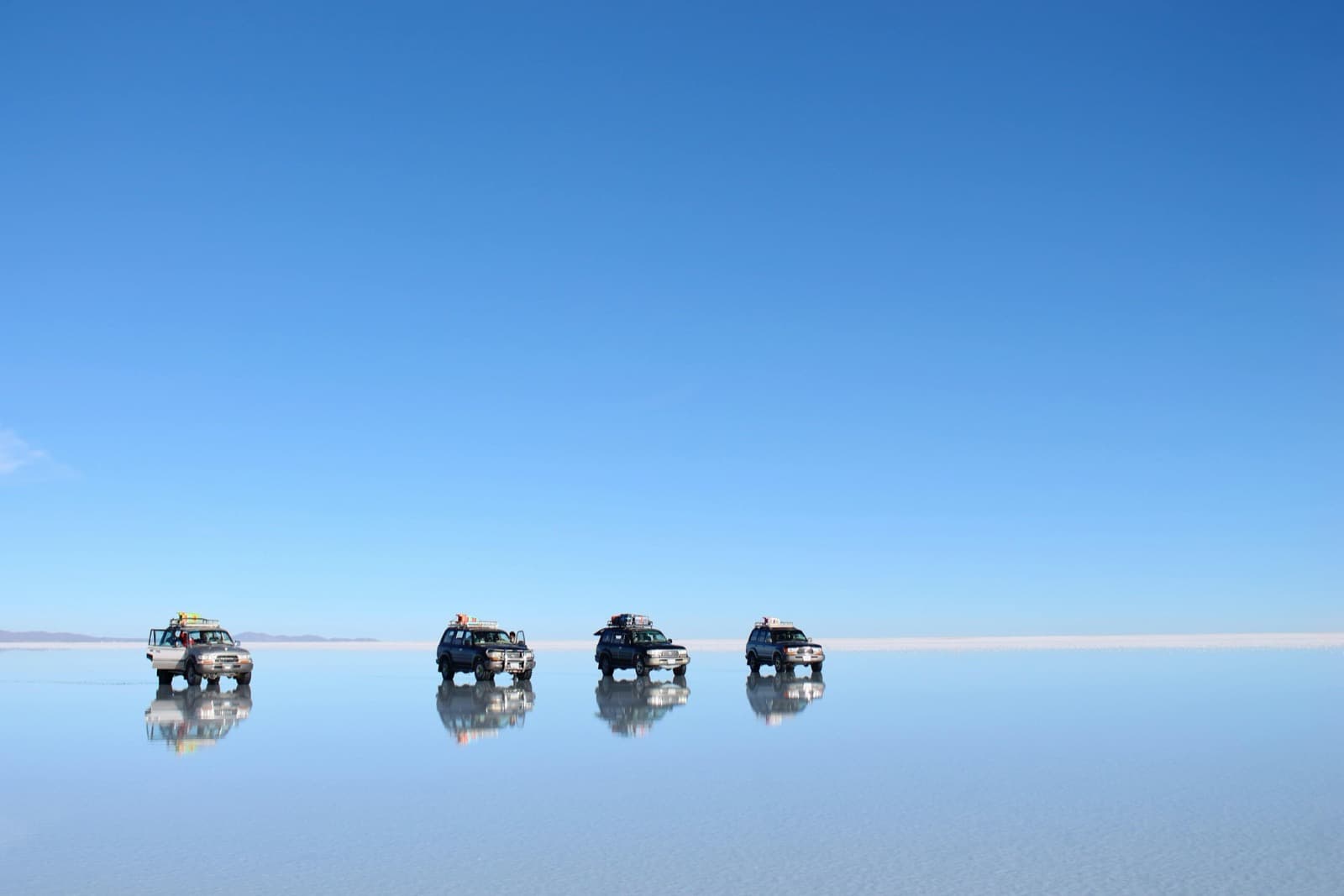 Four 4x4s in a row and their reflection on the Salar de Uyuni turned into a mirror after the rain