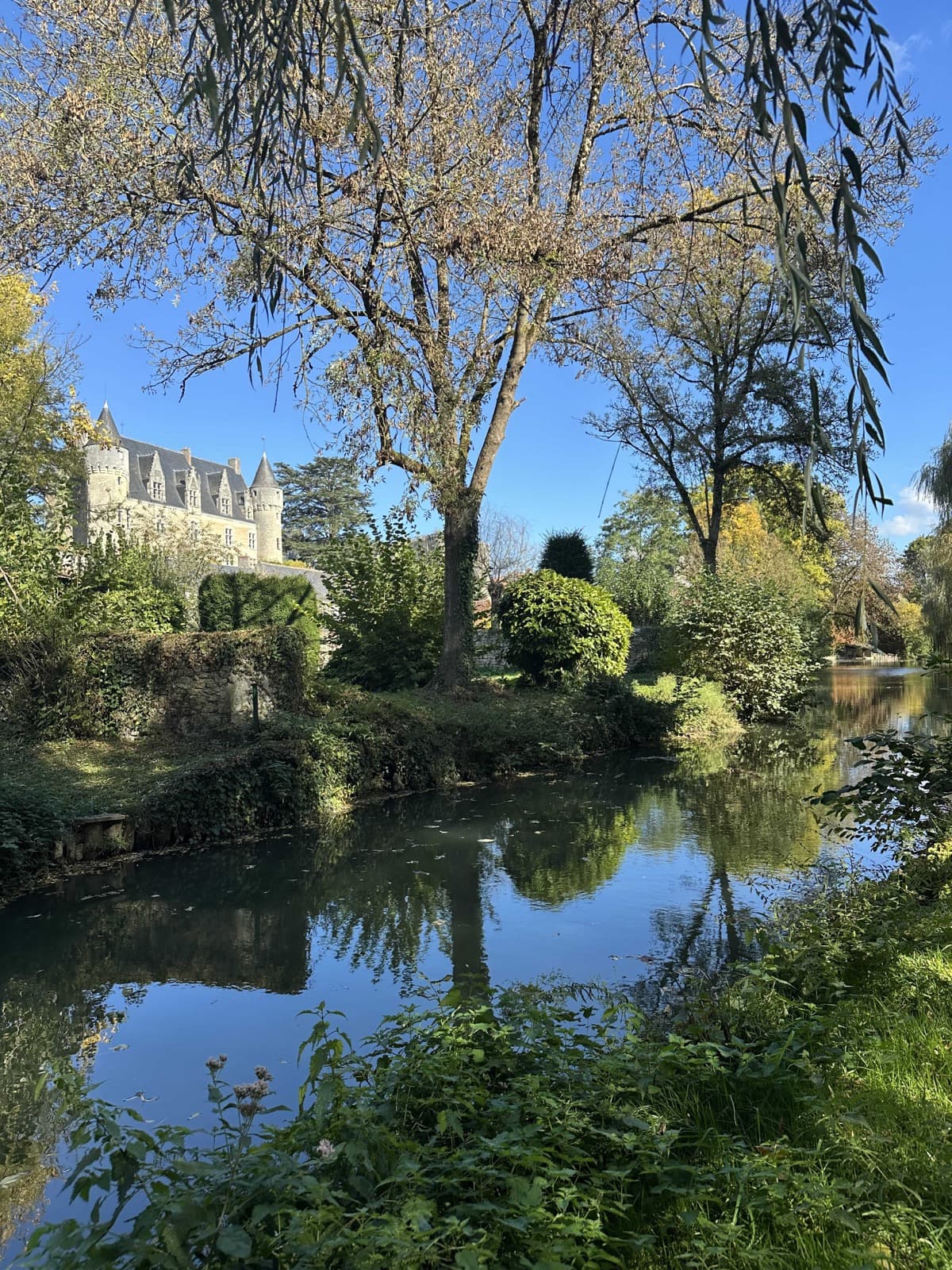 Château de Montrésor reflected in the river lined with trees in autumn colours
