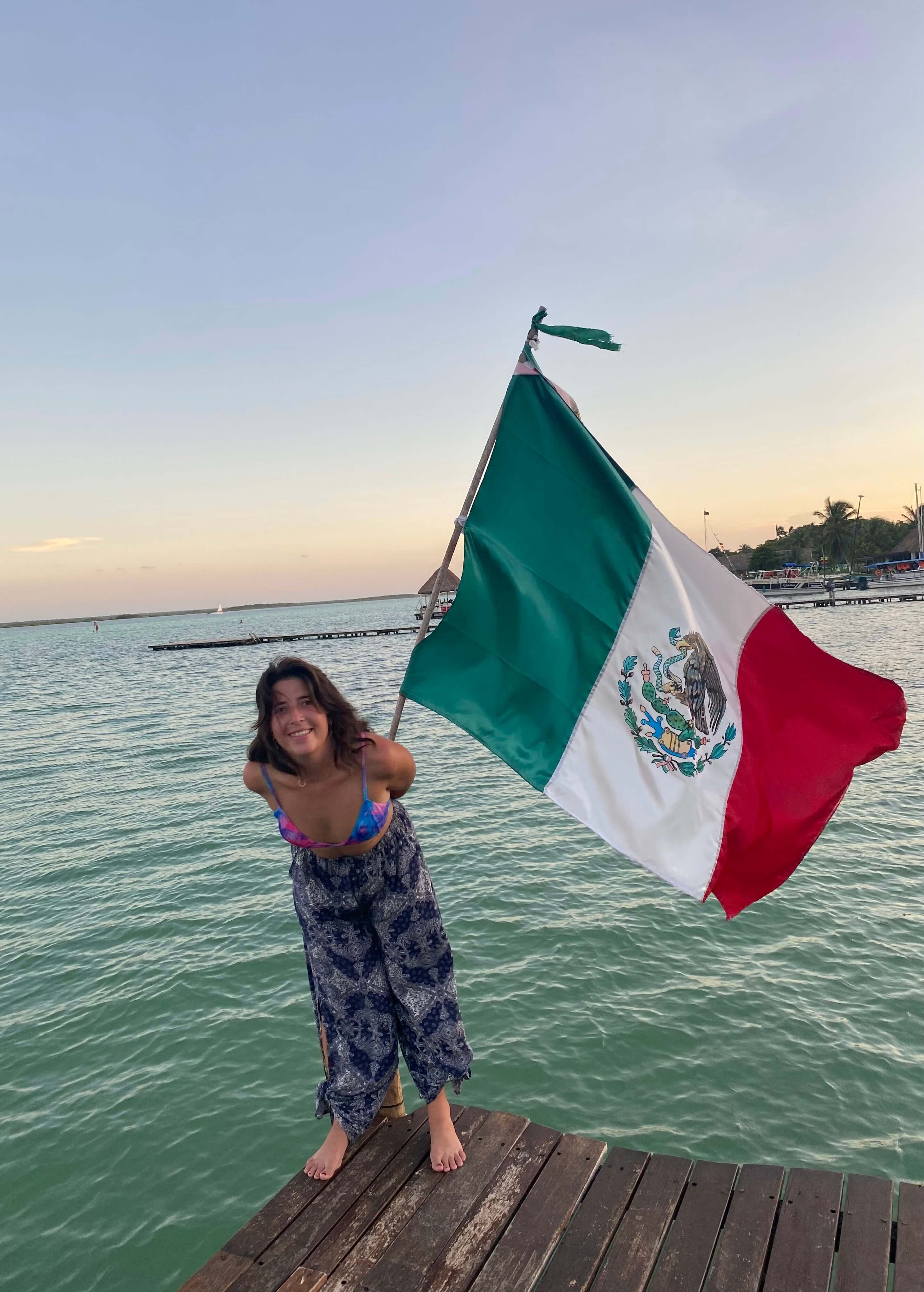 Maïlys tenant un drapeau mexicain coloré dans une rue animée du Mexique