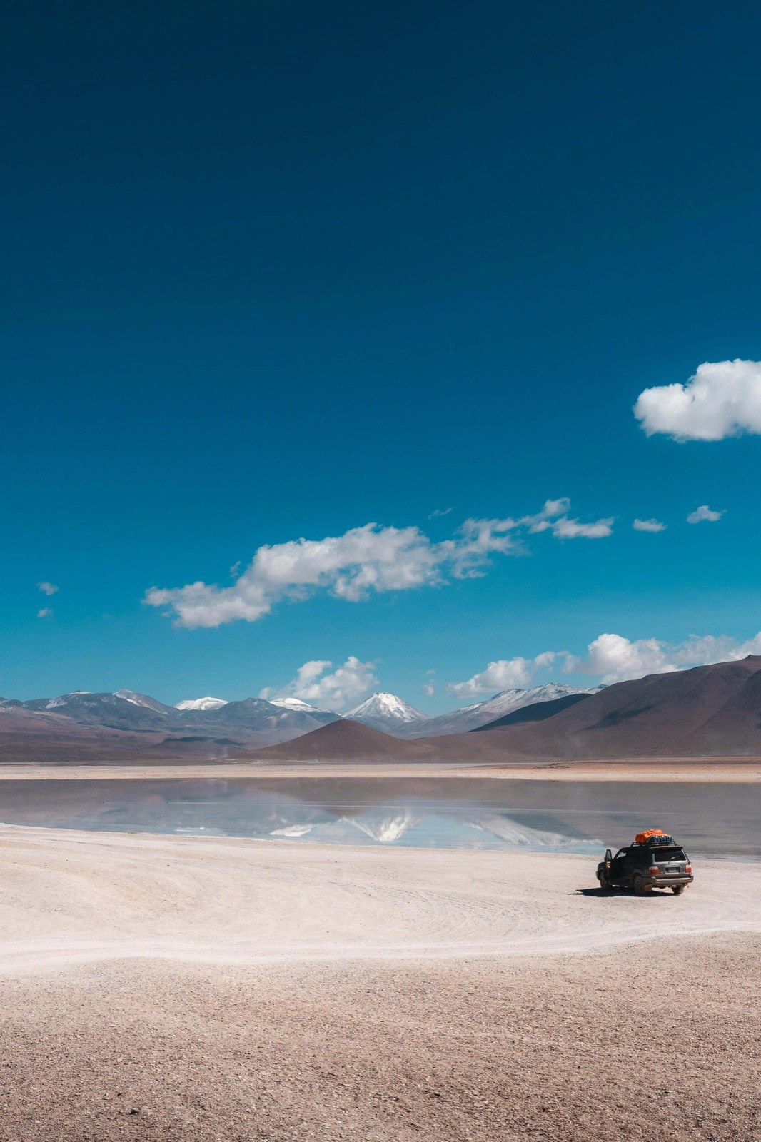 Lagune d'altitude et montagnes enneigées du Sud Lípez avec un 4x4 sur la rive en Bolivie