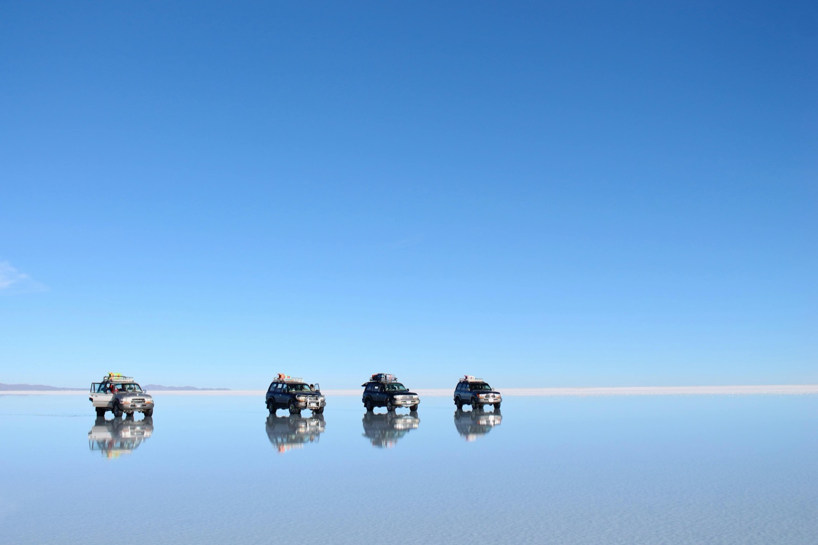 Quatre 4x4 alignés et leur reflet sur le Salar d'Uyuni transformé en miroir après la pluie