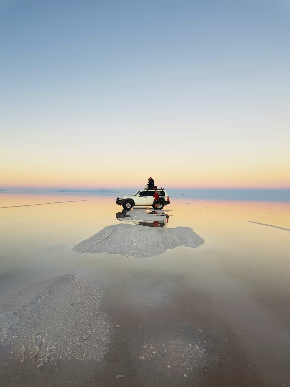 Coucher de soleil sur le Salar d'Uyuni inondé, un 4x4 et son reflet sur le miroir de sel