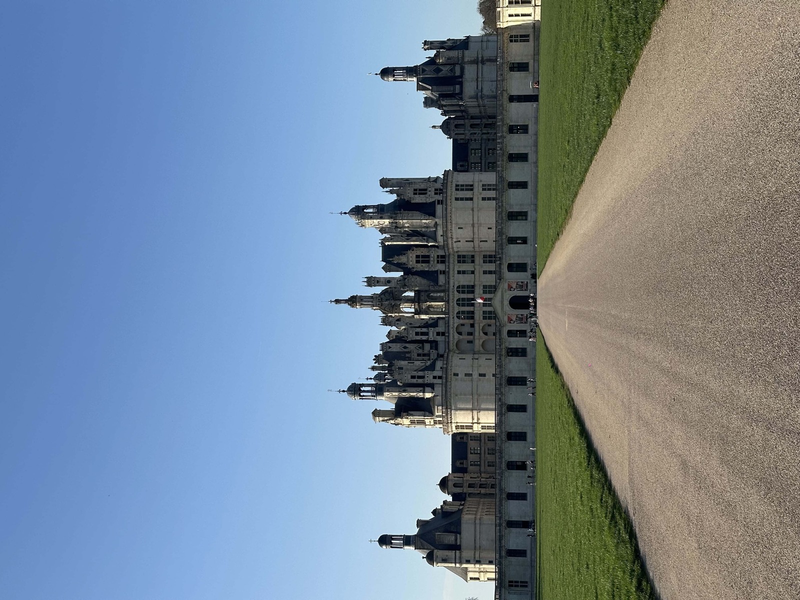 Façade du château de Chambord vue depuis l'allée centrale sous un ciel bleu